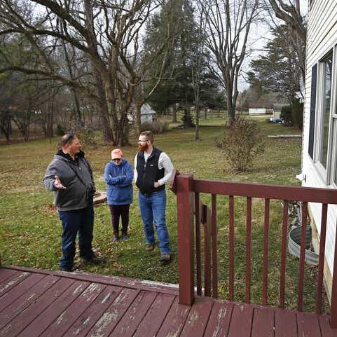 Three people standing on a porch looking at something.